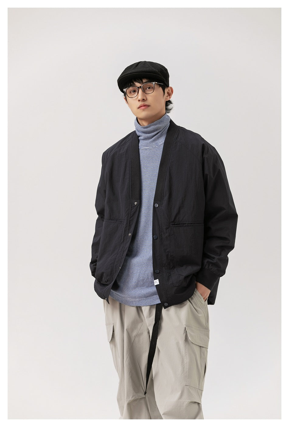 Model wearing a black V-neck snap-front jacket over a striped turtleneck with light gray cargo pants