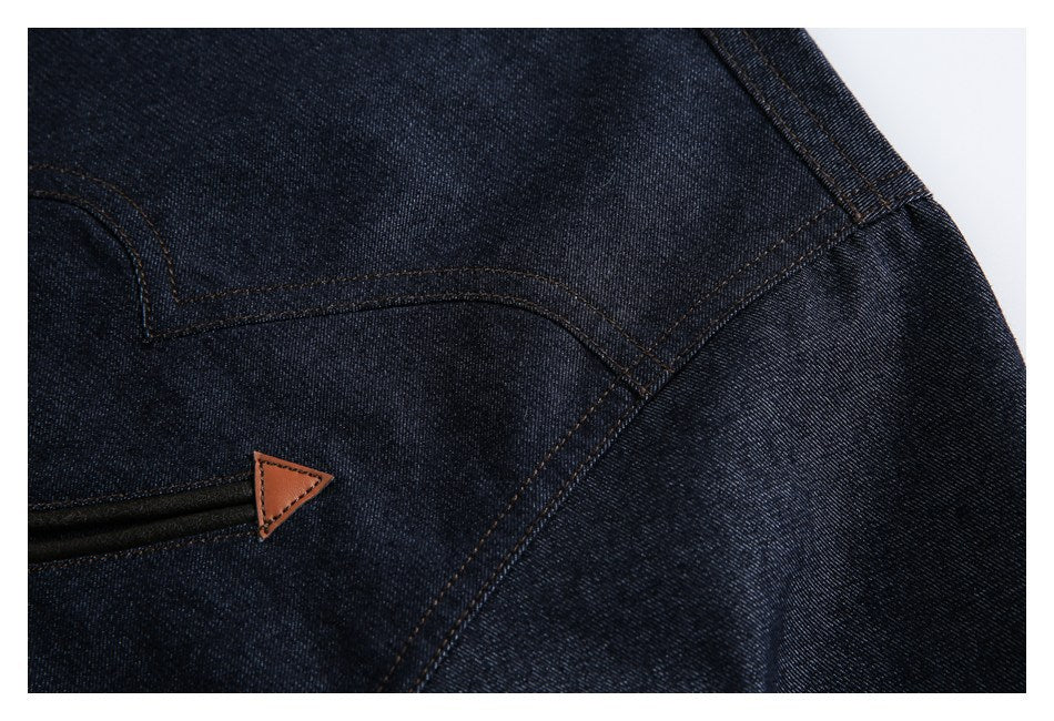 Close-up of dark indigo denim with curved brown stitching and a small tan triangular tab beside a black slit.
