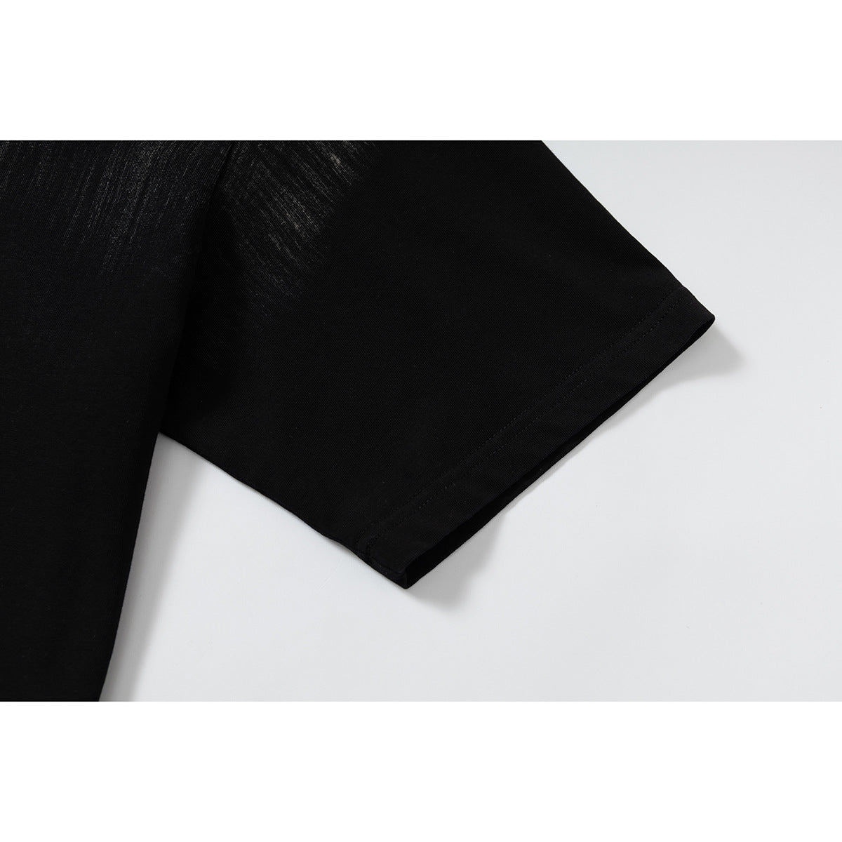 Close-up of a black T-shirt's short sleeve and stitched hem against a white background.