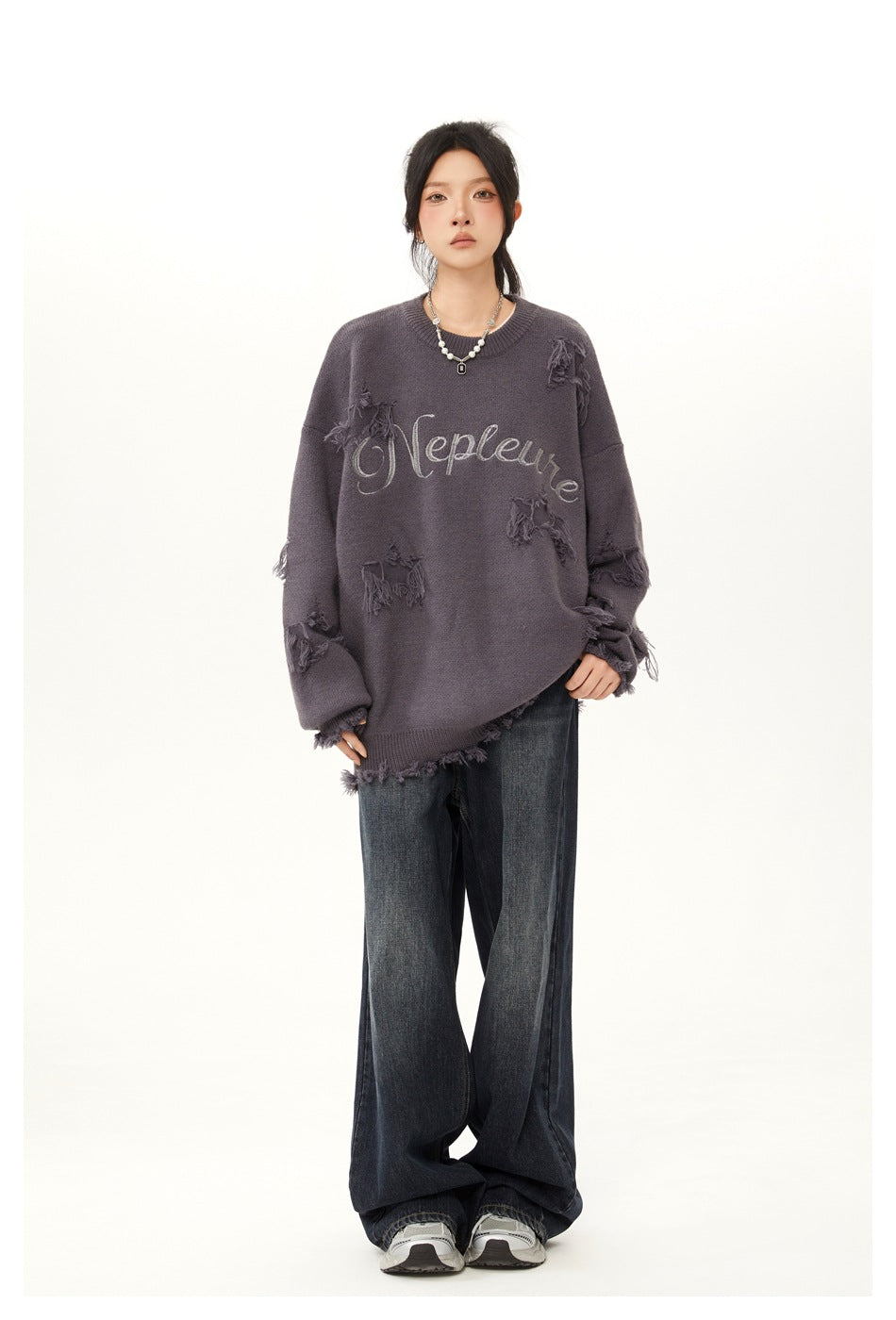 Model wearing an oversized gray distressed knit sweater with embroidered lettering, dark jeans and sneakers