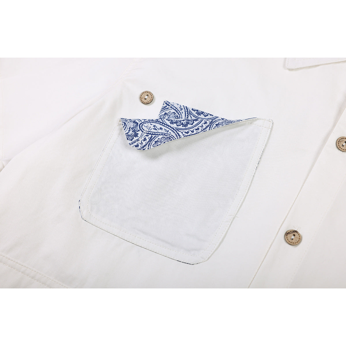 Close-up of an ivory shirt pocket with blue paisley-patterned trim and tan buttons.