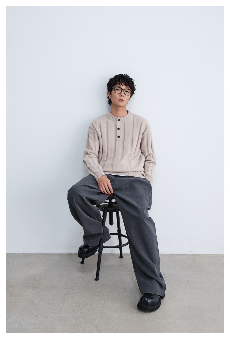 Model seated wearing a light beige sweater with vertical ribbed panels and a three-button neck.