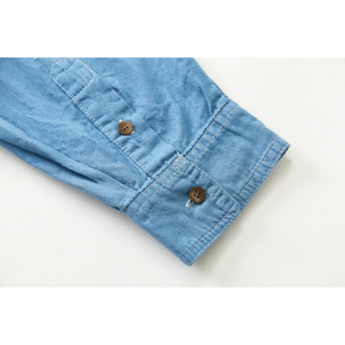 Close-up of a light blue shirt sleeve cuff with two brown buttons and visible stitching.