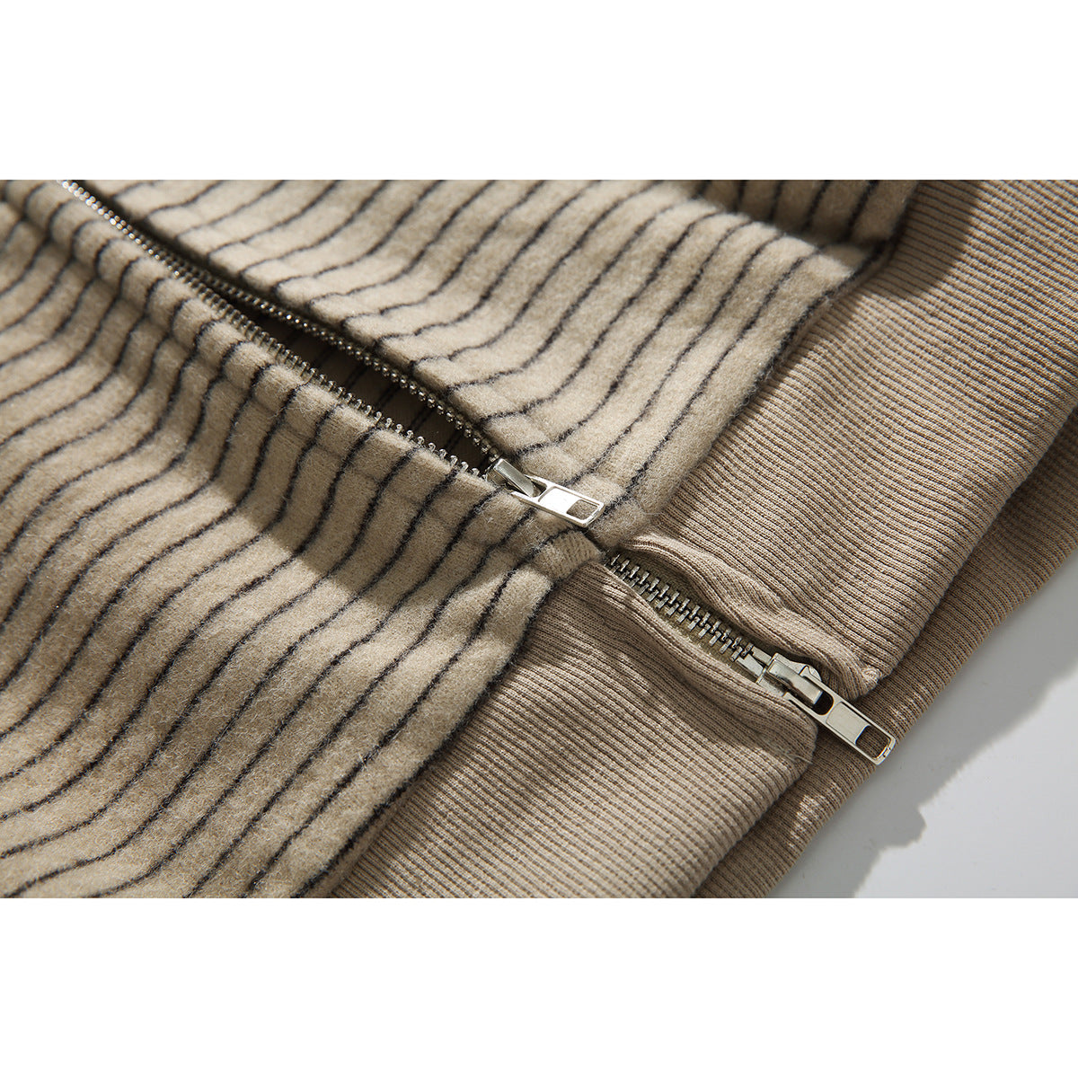 Close-up of the beige pinstriped hoodie’s metal front zipper and ribbed hem.