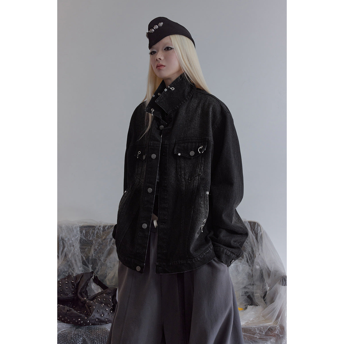 Model wearing an oversized black denim jacket with silver hardware and a tall collar.
