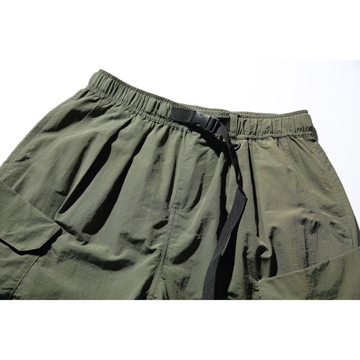 Close-up of olive cargo shorts showing the elastic waistband, black buckle belt, and front pockets.
