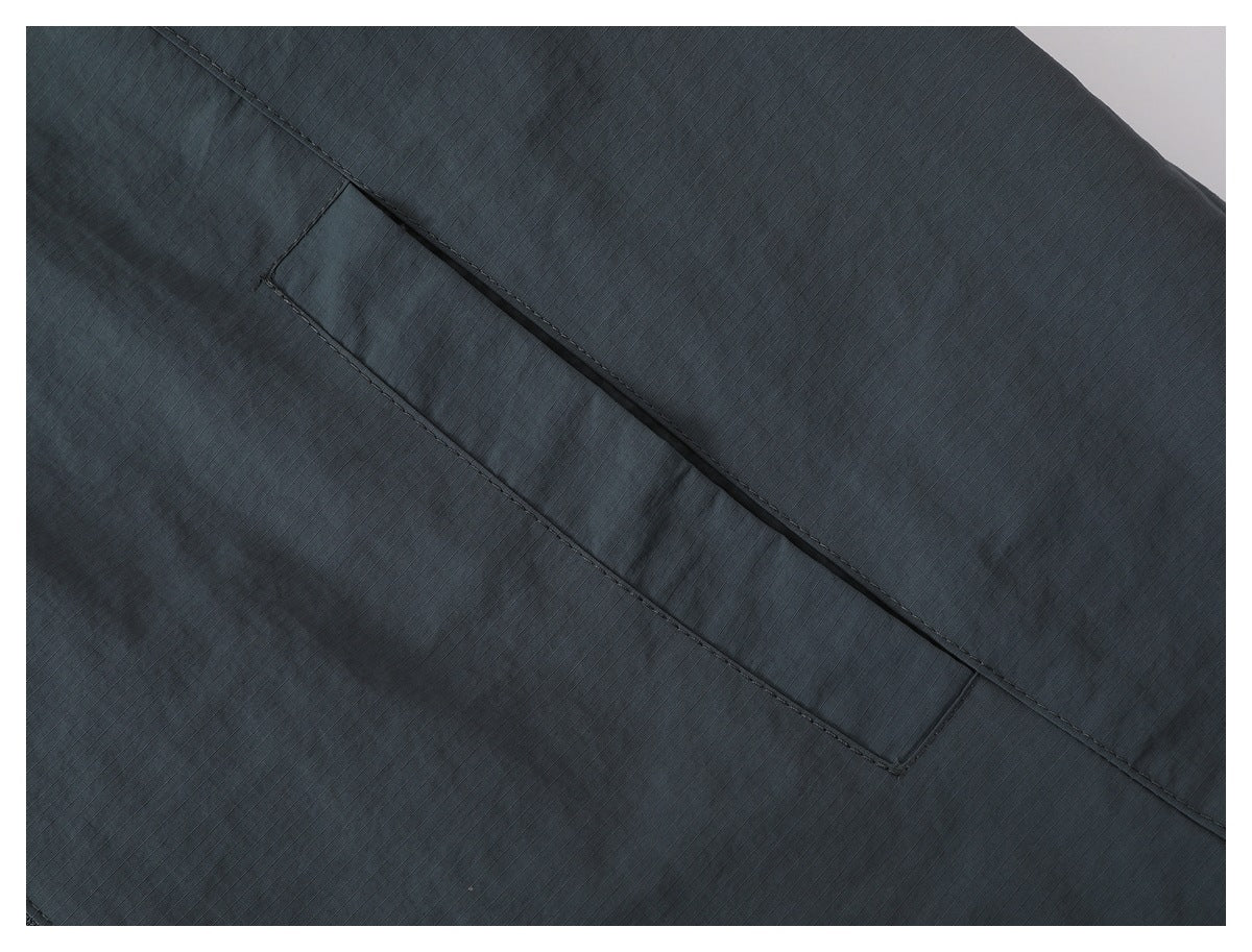 Close-up of a concealed slit pocket on charcoal gray ripstop jacket fabric.