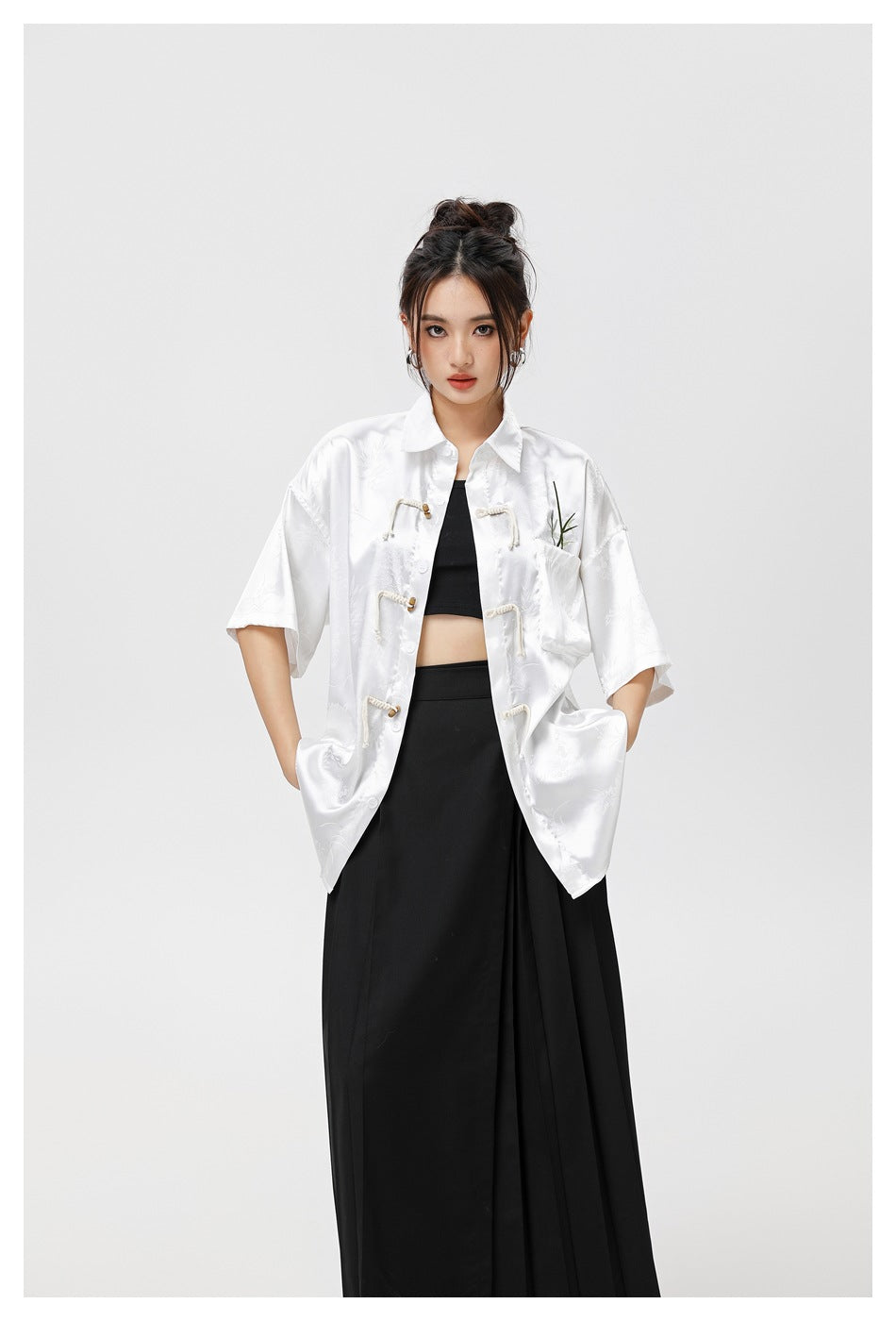Model wearing an open white patterned shirt with frog closures over a black top and long skirt.
