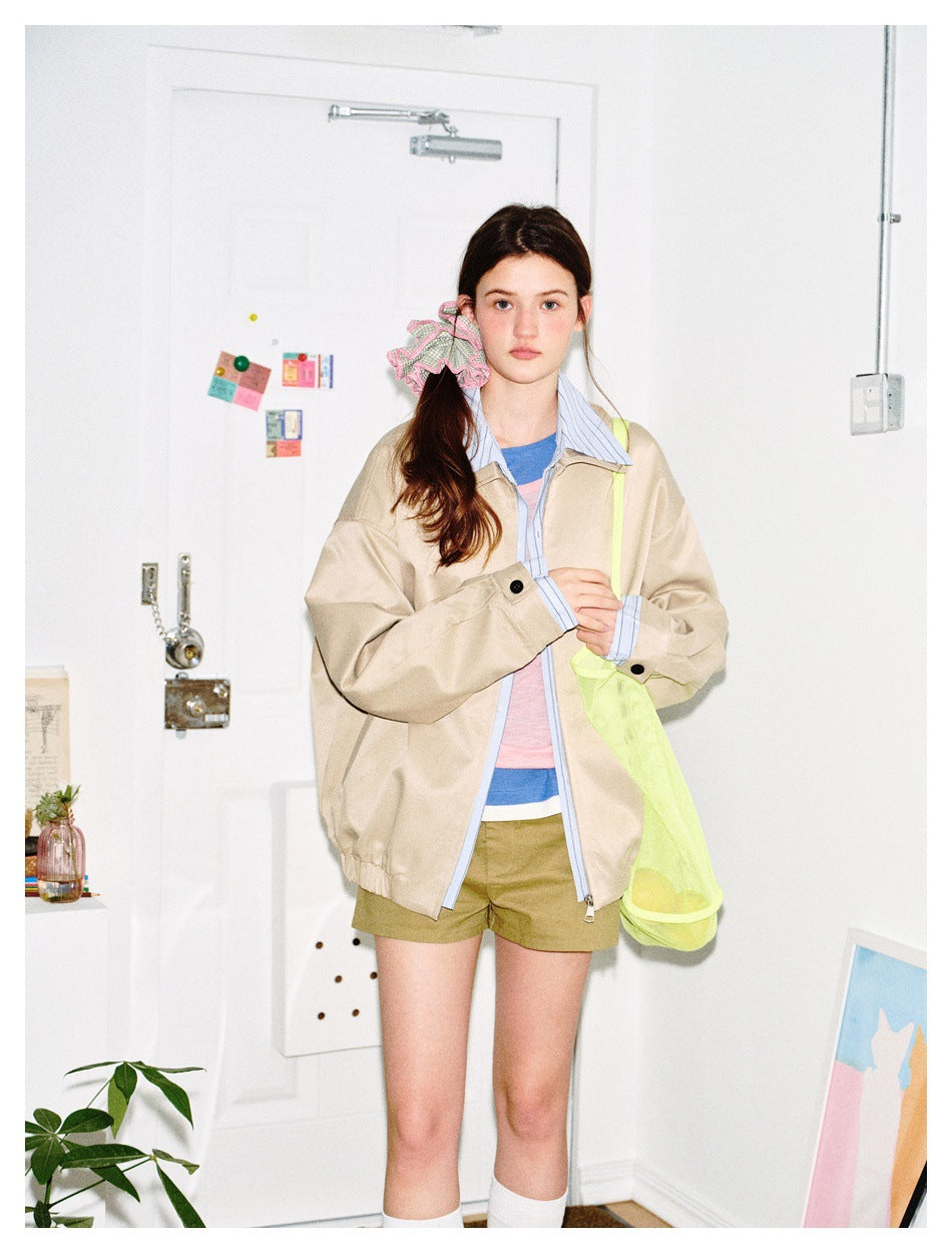 Model standing in a beige oversized jacket with striped collar and button cuffs, with a neon mesh bag and khaki shorts
