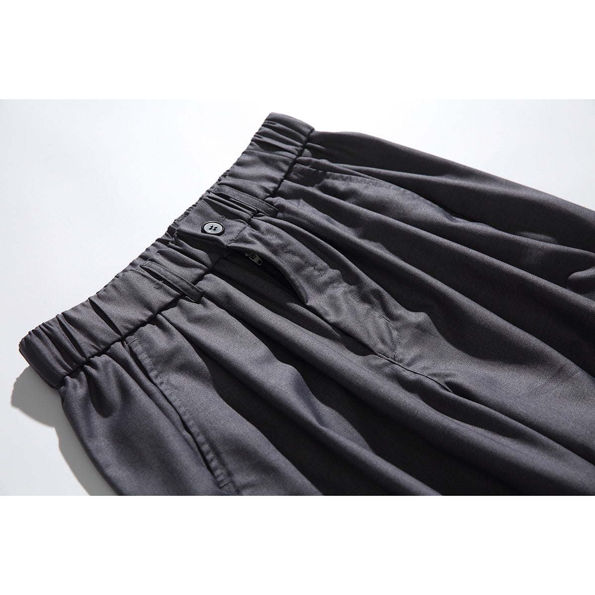 Close-up of charcoal-gray trousers showing the elasticated waistband, button, fly, and pleats.