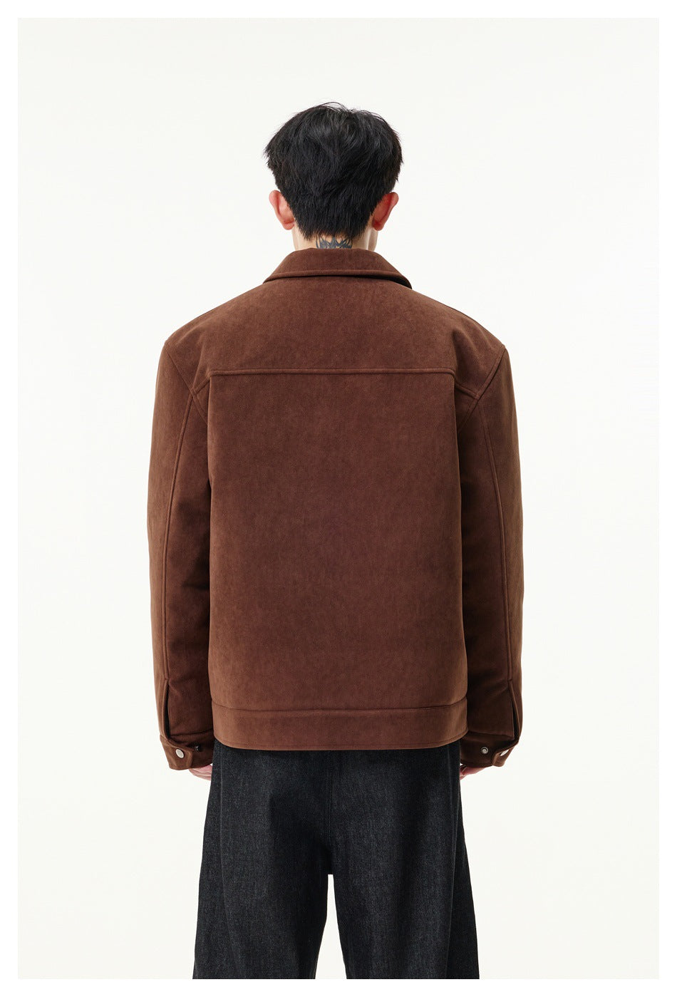 Rear view of a model wearing a brown collared jacket with a horizontal back yoke and buttoned cuffs.