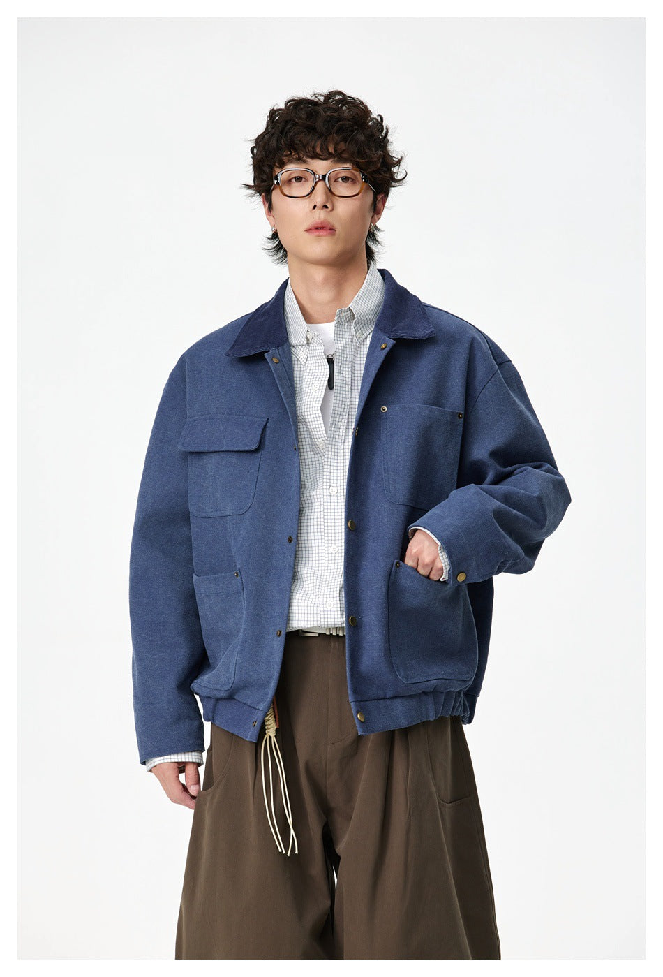 Full-length front view of a model wearing a blue utility jacket with multiple pockets and wide brown trousers.