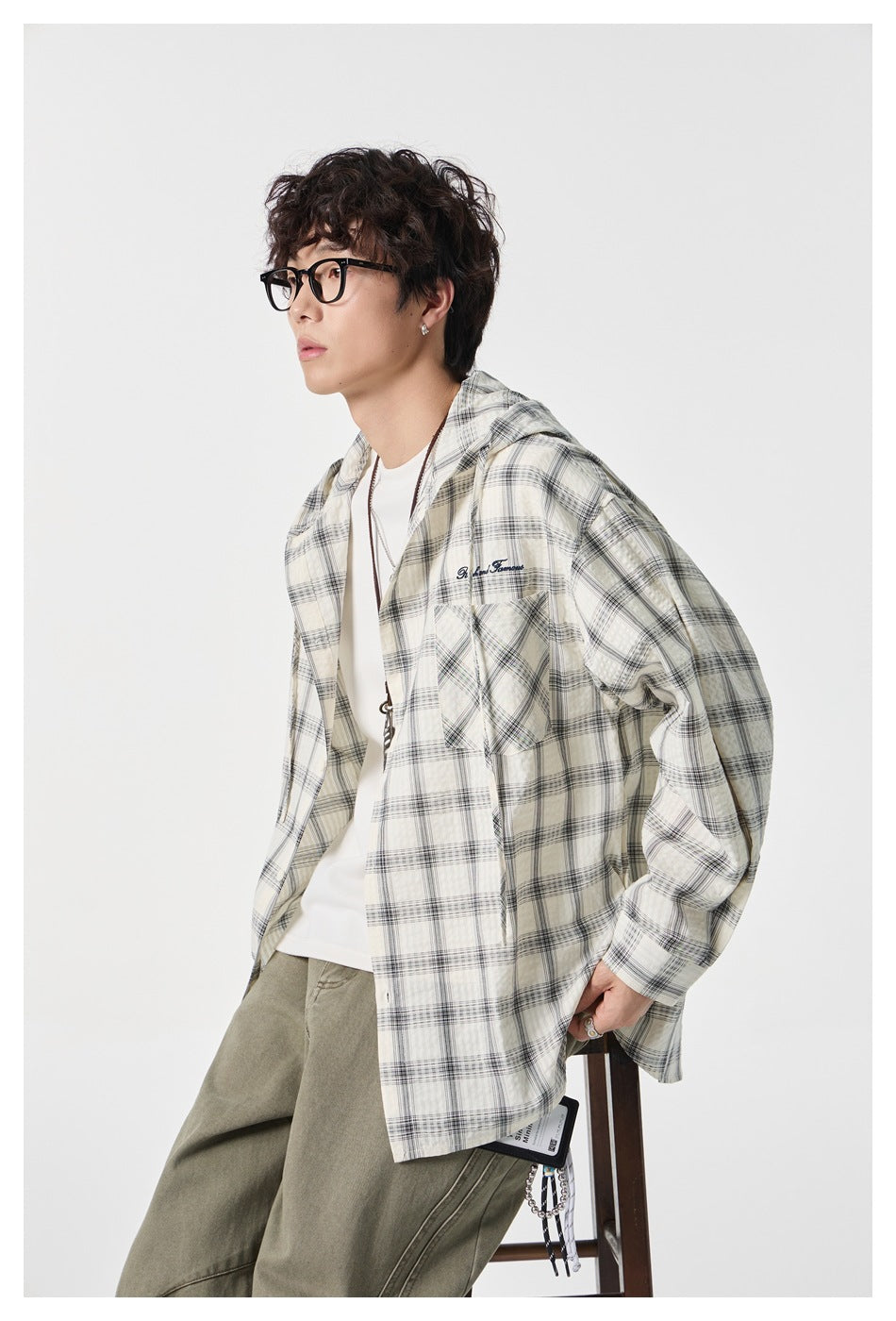 Close view of a model wearing an open cream and gray plaid hooded shirt with a chest pocket.