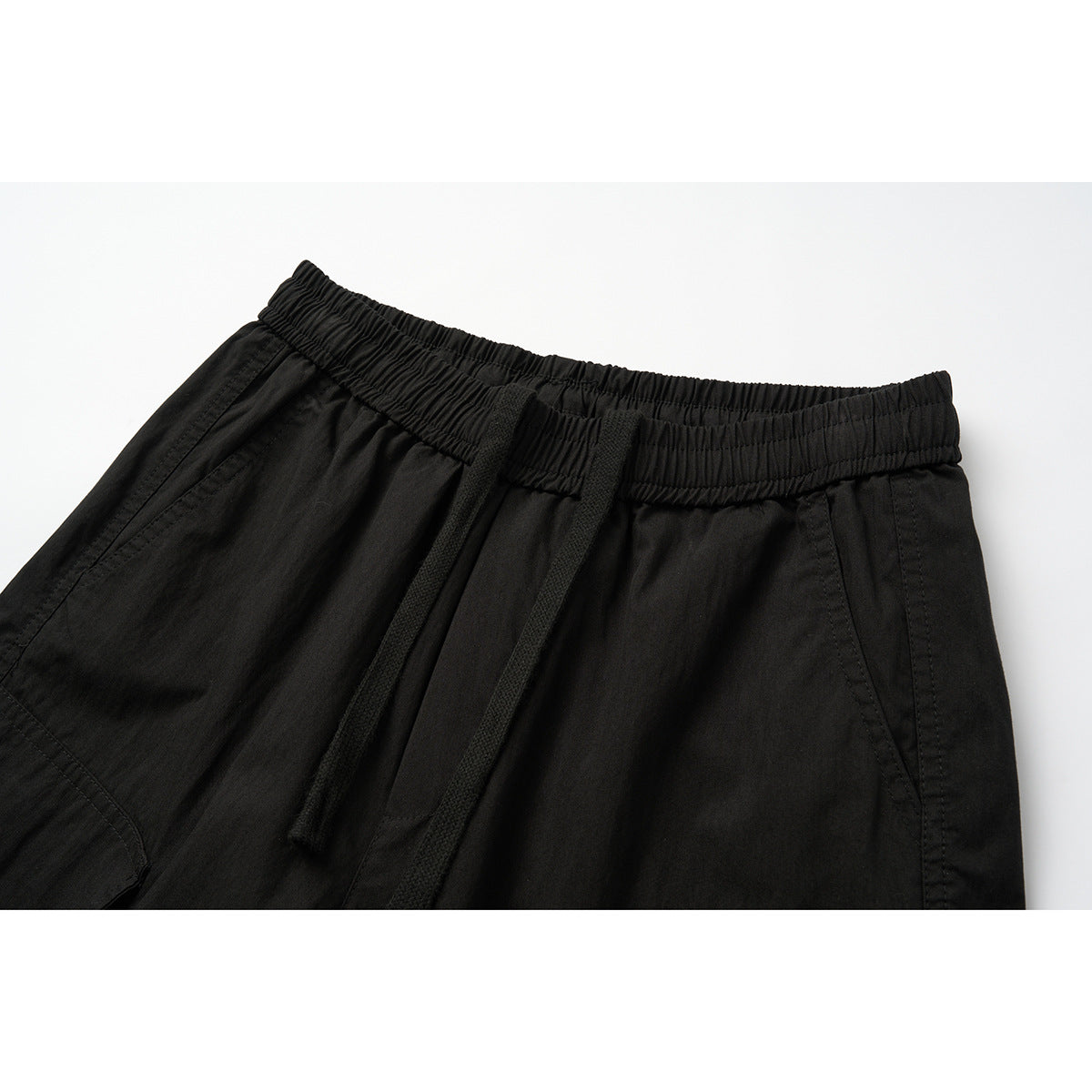 Close-up of black cargo pants showing the elastic waistband, drawstring, and angled front pockets.