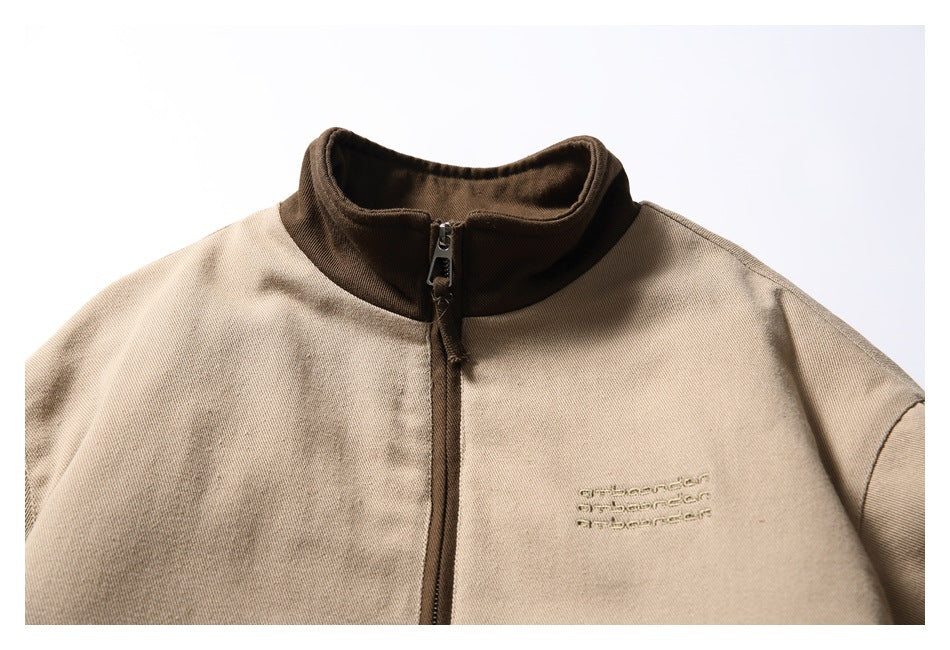 Close-up of a tan jacket front with a dark brown stand collar, center zipper, and small embroidered chest text.