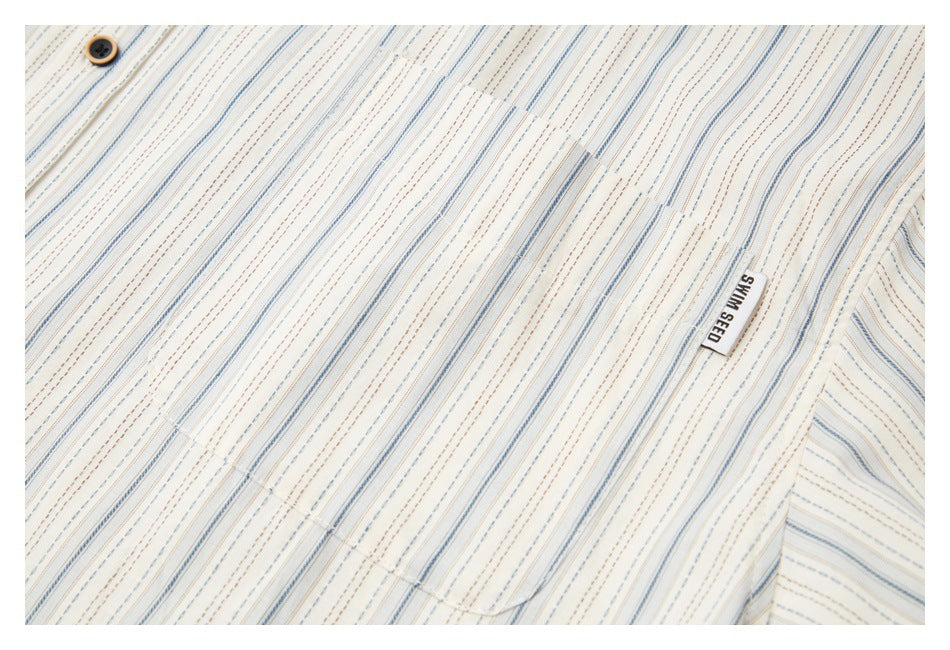 Close-up of cream fabric with fine blue and brown stripes, a dark button, and a small sewn label.