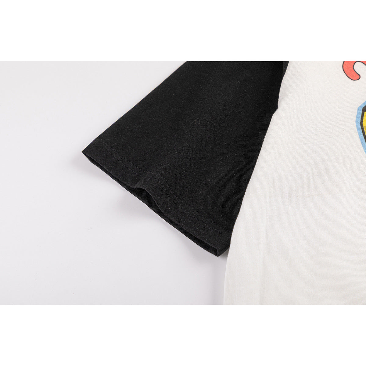 Close-up of the black sleeve hem and seam beside the off-white body of a raglan T-shirt.