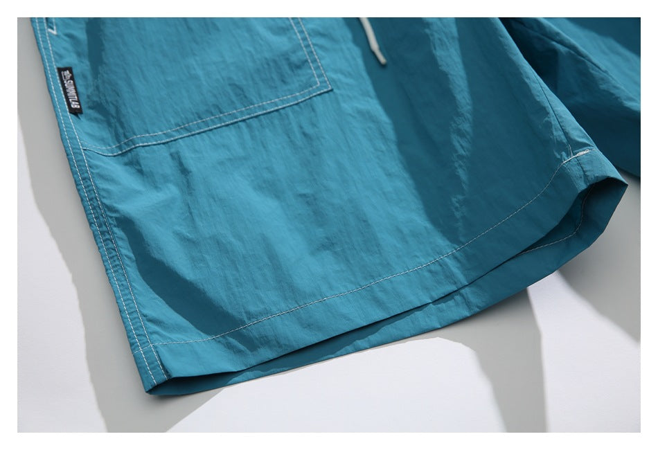 Close-up of teal shorts with a large patch pocket, stitched hem, and a small black garment tag.