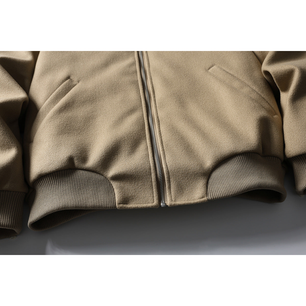 Close-up of the tan jacket's front zipper, slanted pockets, and ribbed hem.