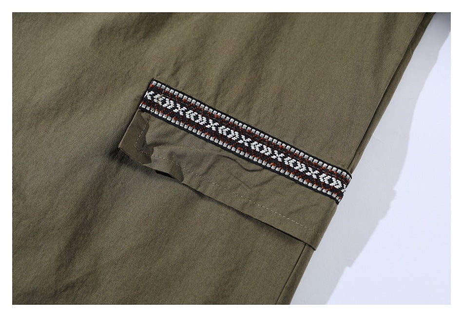 Close-up of an olive shirt sleeve with a black, white, and rust geometric trim band.