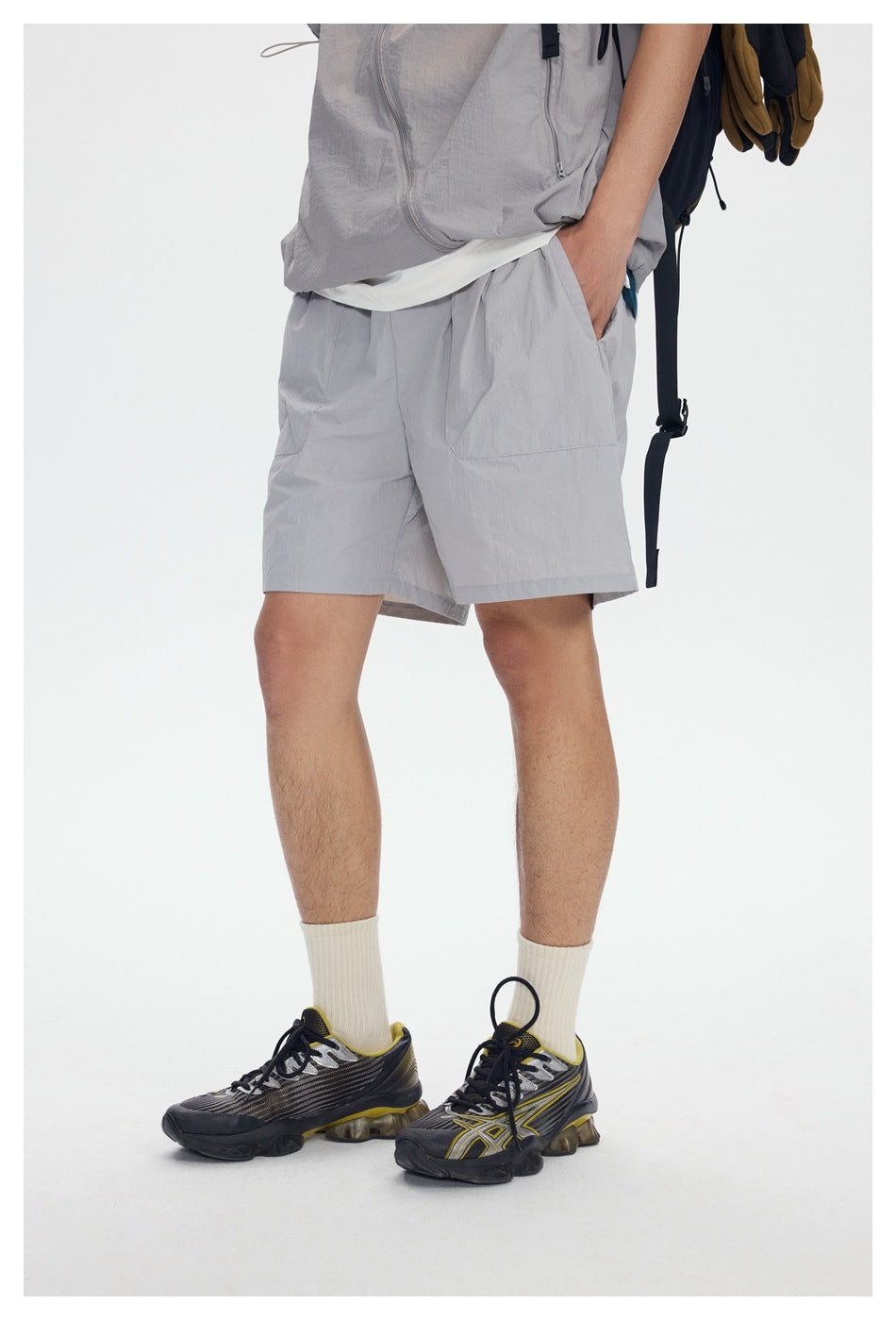 Model wearing light gray relaxed shorts with hand in pocket, cream socks and sneakers, cropped front view
