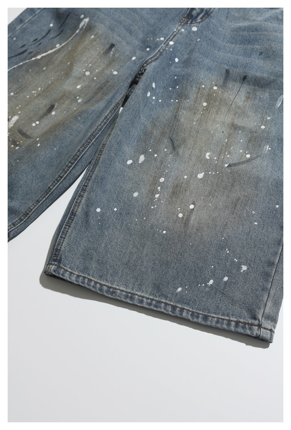Close-up of blue-gray jeans with scattered white paint splatters and a stitched hem.