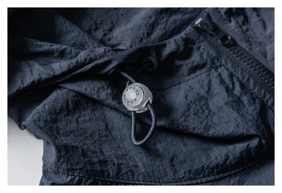 Close-up of a dark jacket's drawcord adjuster and zipper; the round adjuster is marked VOGUE.
