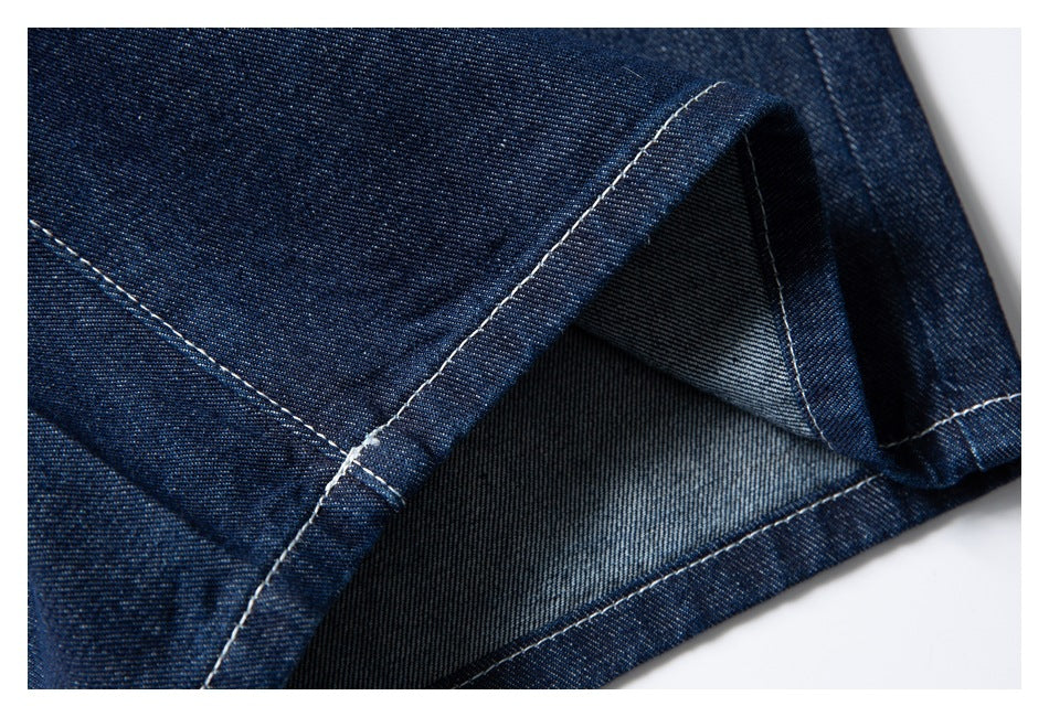 Close-up of a dark indigo denim shorts leg hem, showing the folded edge, white stitching, and reverse fabric.