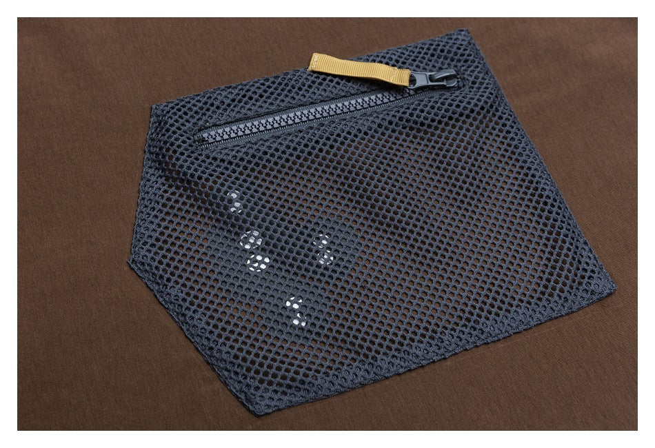 Close-up of a dark mesh pocket on a brown shirt, with a black zipper and tan pull tab.