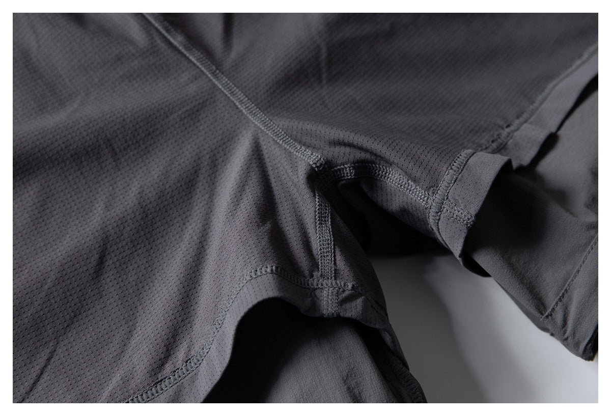 Close-up of dark charcoal perforated garment fabric showing curved seams and stitched construction.