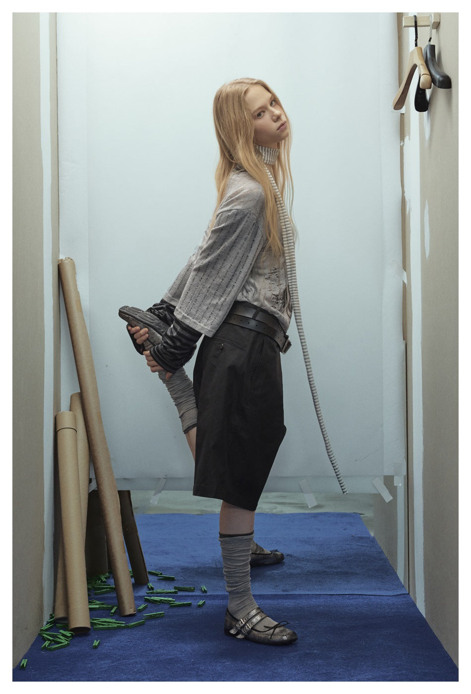 Model in side pose wearing the gray striped-sleeve layered top with black shorts and a belt