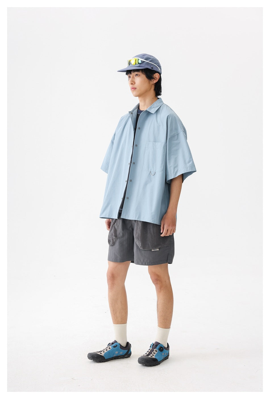 Model wearing a pale blue oversized short-sleeve button-up shirt with a chest pocket, viewed from the front at an angle.