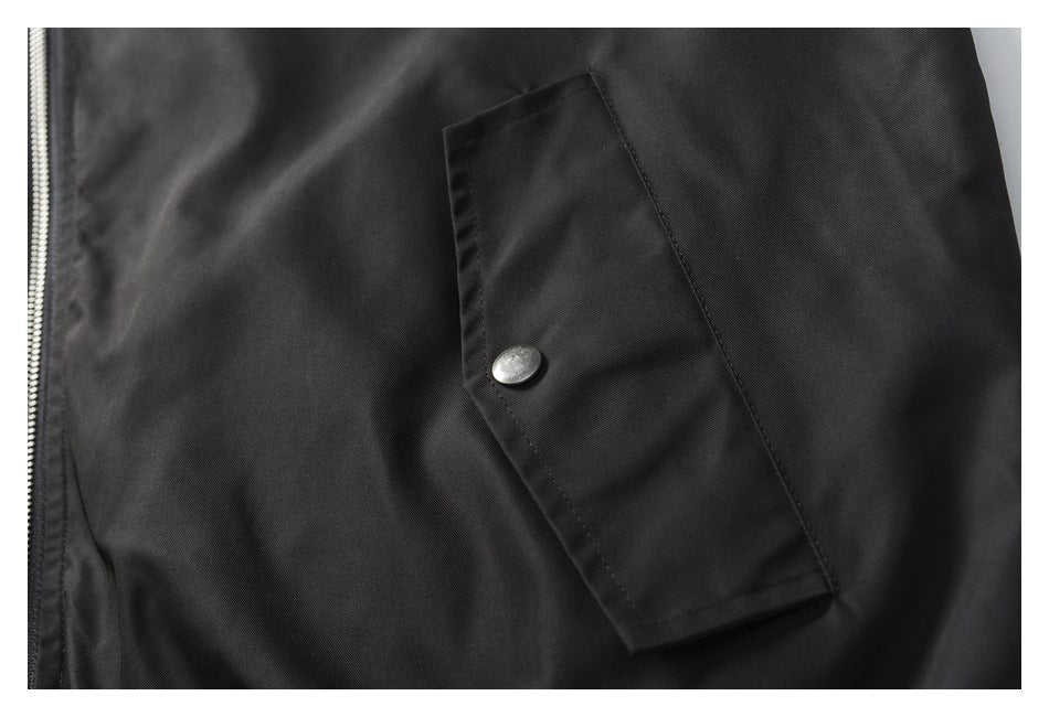 Close-up of a black jacket pocket flap with a silver snap beside the front zipper.