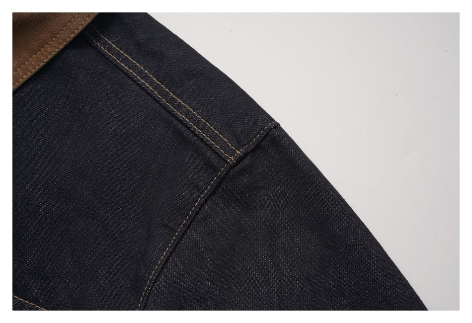Close-up of dark denim jacket shoulder and seam stitching against a light background.