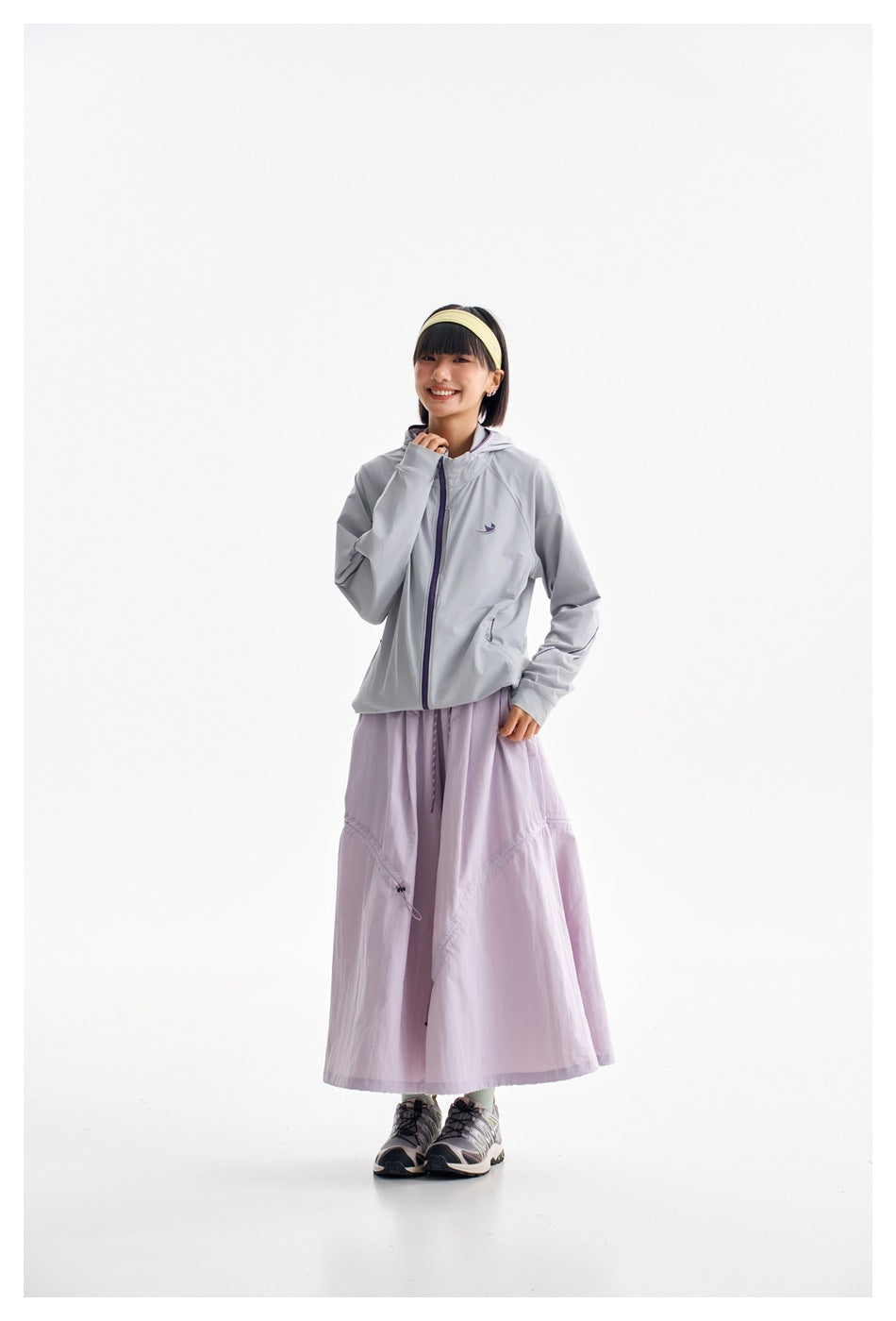 Model wearing a light gray hooded zip jacket with purple trim and a lavender ankle-length skirt.
