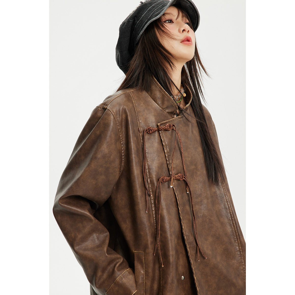 Close view of a model wearing a brown jacket with a stand collar and knotted cord closures.