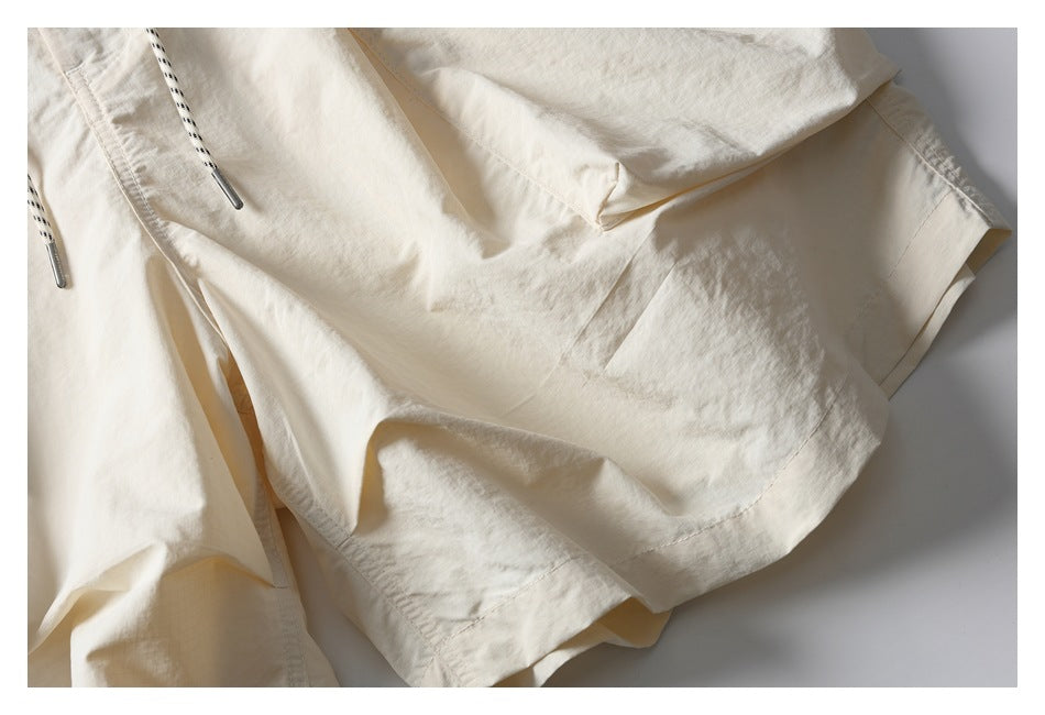 Close-up of the ivory shorts' loose leg and stitched hem, with part of the black-speckled drawstring visible.