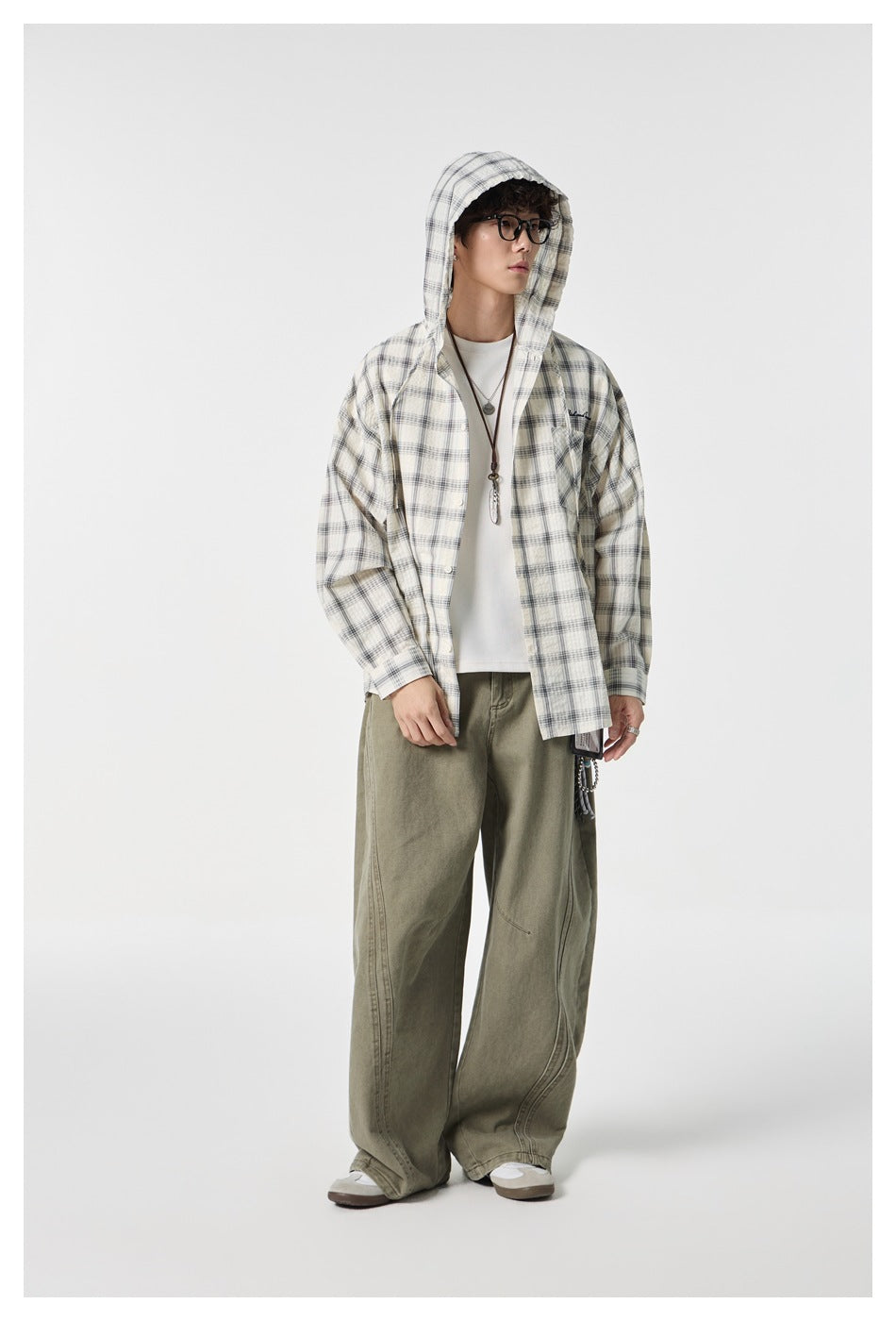 Model wearing cream plaid hooded shirt open over white tee with hood up and olive wide-leg pants