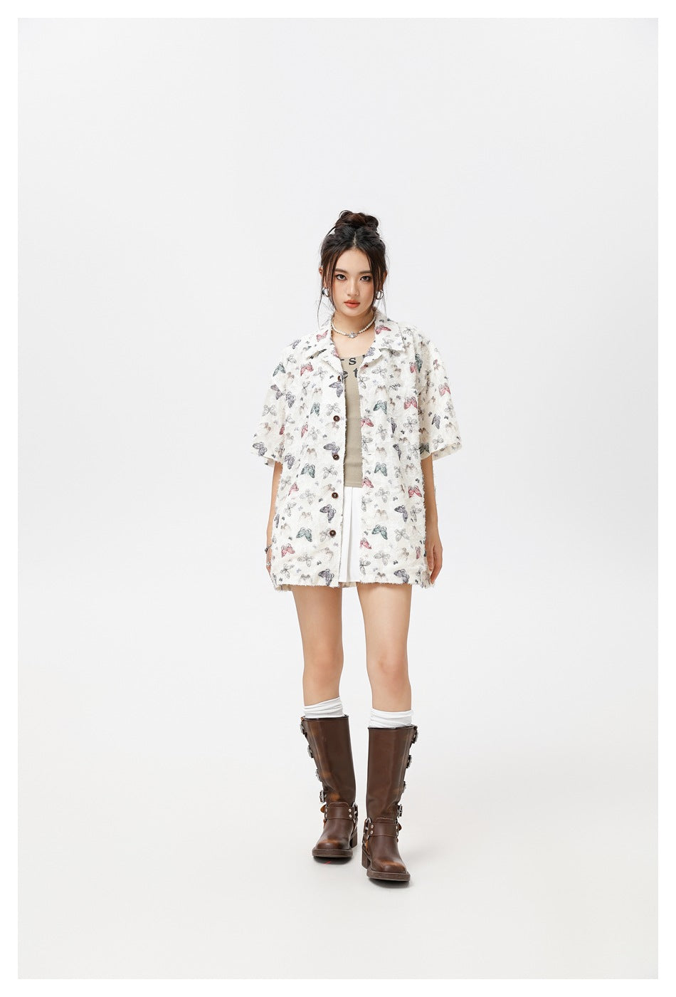 Model wearing the off-white butterfly print short-sleeve shirt open over a tank top, white pleated skirt and brown boots