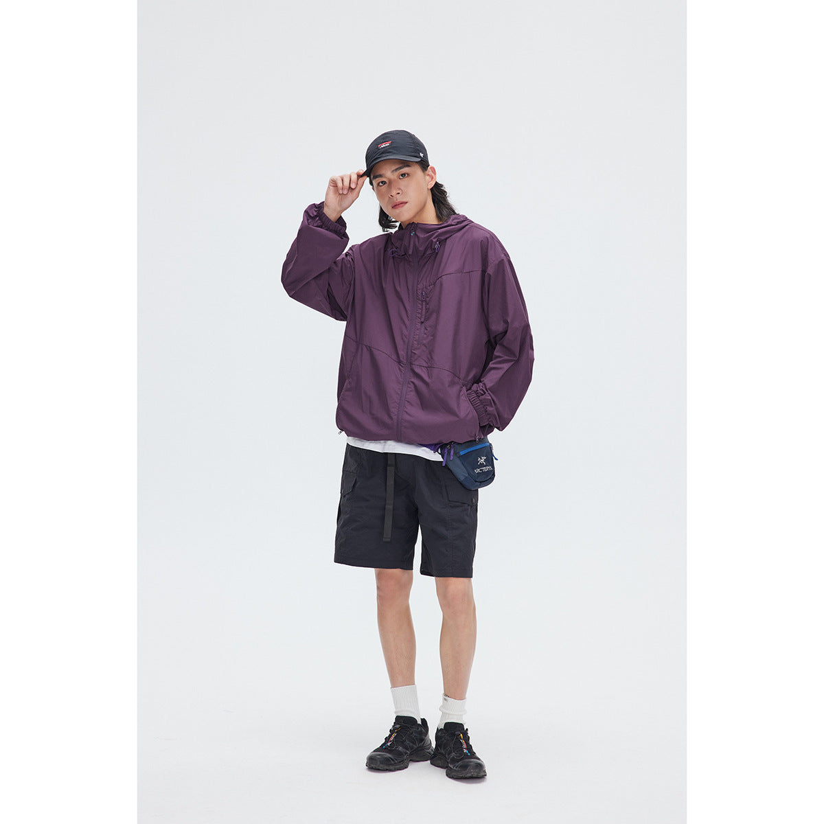 Full-length model wearing a plum hooded jacket with black shorts and a cap.