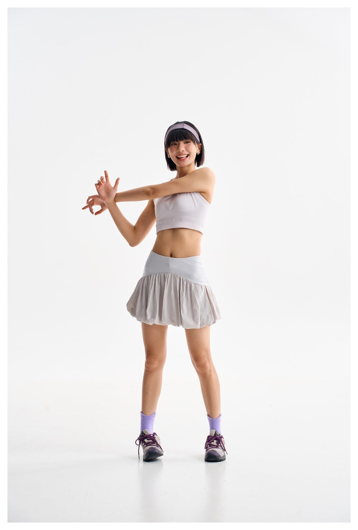 Model in a light gray bubble-hem skirt and white cropped top, stretching her arms.
