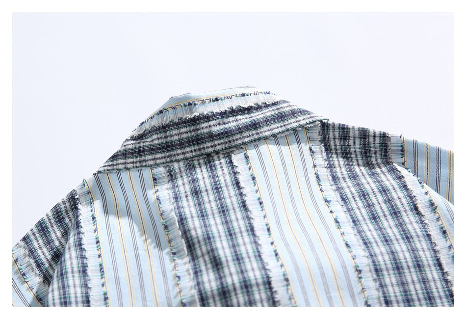 Close-up of a shirt collar and shoulder in light blue fabric with dark plaid and striped bands.