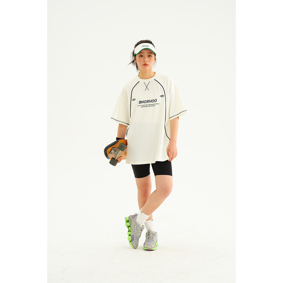 Model wearing an oversized white athletic T-shirt with dark piping and black cycling shorts, shown from the front.