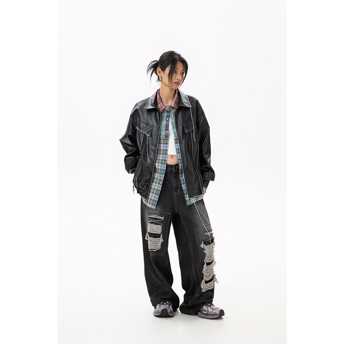 Model wearing an oversized black jacket with white stitch details over a colorful plaid shirt.
