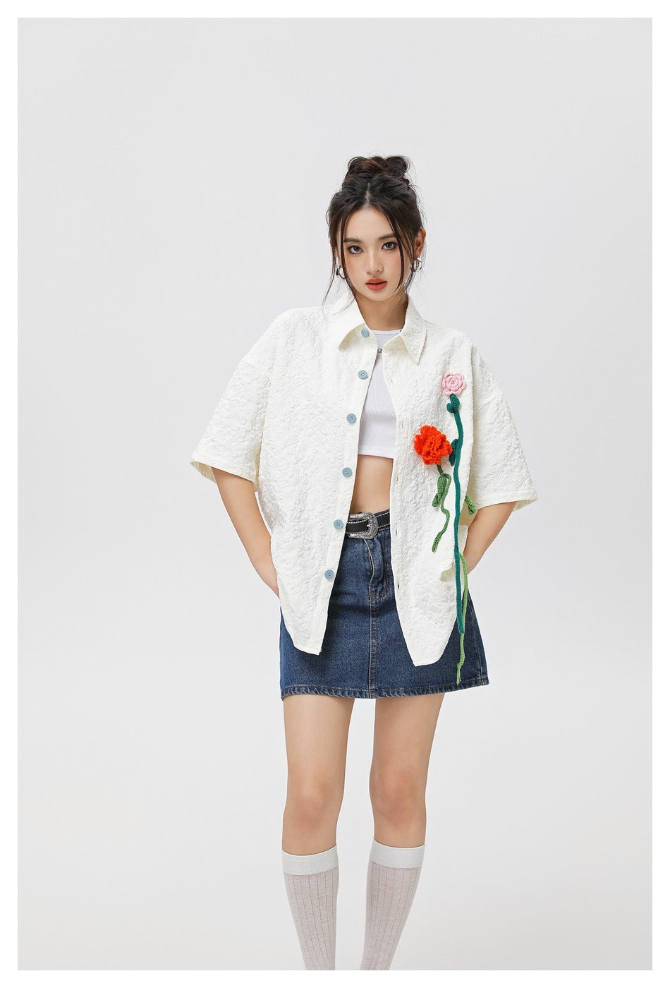 Front view of a model in a white textured short-sleeve shirt with colorful flower appliqués and a denim skirt.