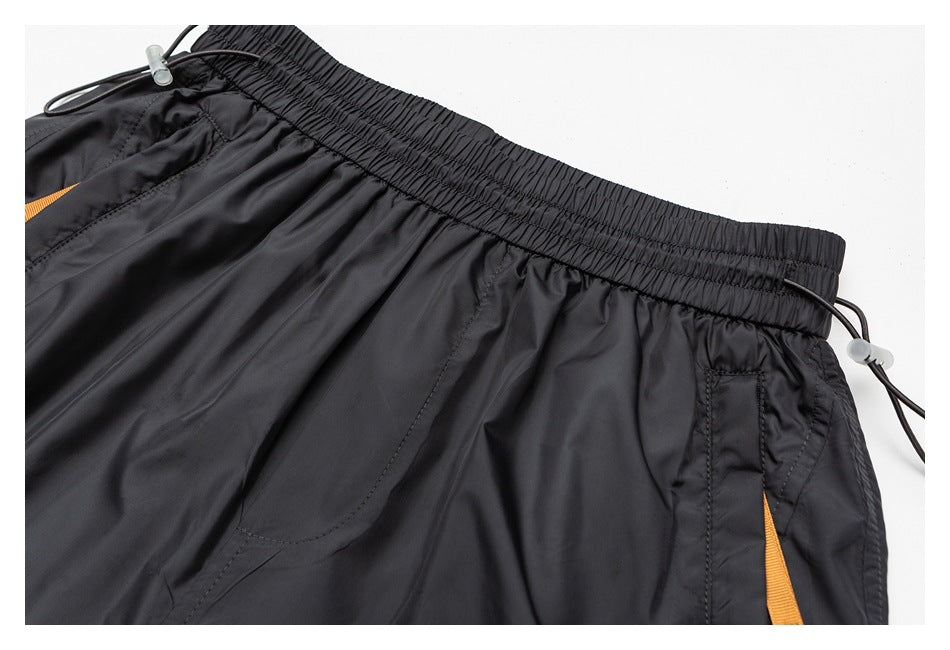Close-up of black shorts showing the elastic waistband, front pocket seams, drawcord, and orange side detail.