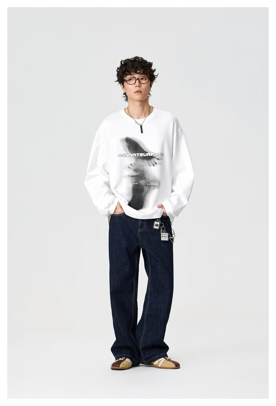 Front view of a model wearing a white long-sleeve shirt with a large gray graphic and dark jeans.