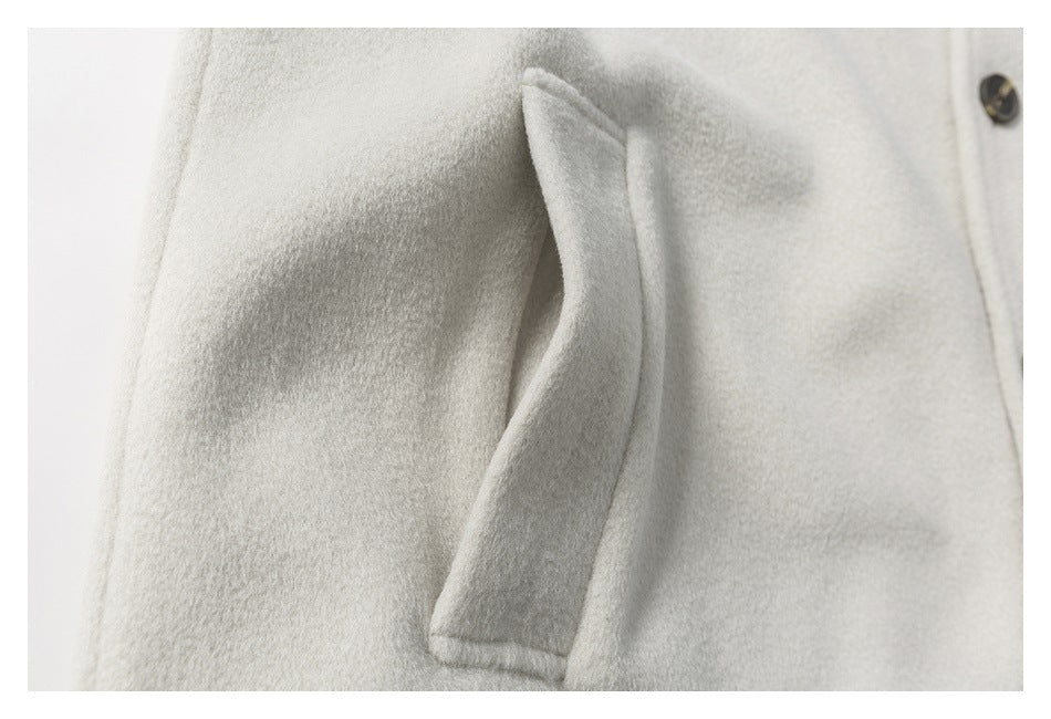Close-up of a slanted welt pocket on an ivory coat beside its buttoned front.