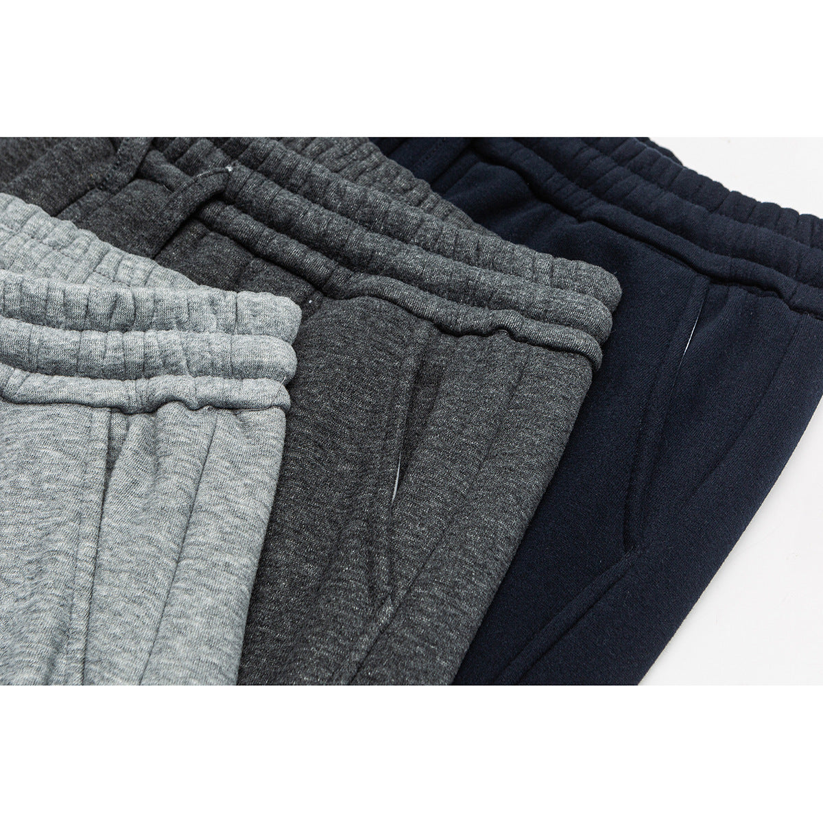 Close-up of gray, charcoal, and navy sweatpants with elastic waistbands arranged together.