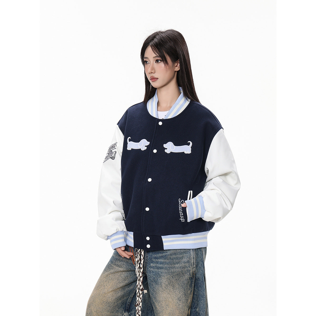 Angled front view of a navy varsity jacket with white sleeves, striped cuffs and dog appliqués on a model.